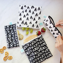 Load image into Gallery viewer, A person zips a Bumkins Reusable Snack Bag, Small 2-Pack: XOXO &amp; Hearts among other bags with sandwiches and snacks on a marble surface.
