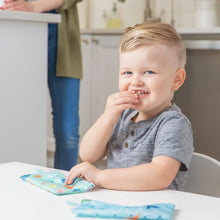 Load image into Gallery viewer, A child smiles while snacking from Bumkins Reusable Snack Bag, Small 2-Pack: Ocean Life &amp; Whale Tail; an adult stands in the background.

