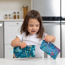 Load image into Gallery viewer, A young girl holds Bumkins Reusable Snack Bag, Small 2-Pack: Jungle &amp; Animal Prints in a bright kitchen.
