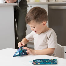 Load image into Gallery viewer, A child eagerly reaches into Bumkins Reusable Snack Bag, Small 2-Pack: Jungle &amp; Animal Prints at a table with an adult in the background.

