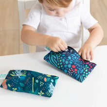 Load image into Gallery viewer, A child in a white shirt examines Bumkins Reusable Snack Bag, Small 2-Pack: Jungle &amp; Animal Prints on a white table.
