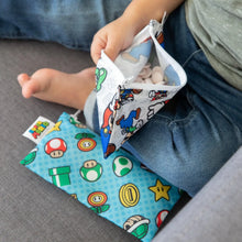 Load image into Gallery viewer, Close-up of a child sitting barefoot on a gray couch with Bumkins Reusable Snack Bag, Small 2-Pack: Super Mario™.
