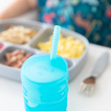 Load image into Gallery viewer, Close-up of Bumkins Silicone Straw Cup with Lid: Blue on a white table, with a gray plate of food and fork blurred in the background.
