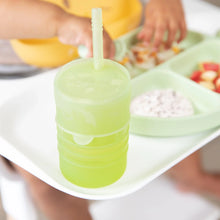 Load image into Gallery viewer, Tiny hands reach for food on a green divided plate as a Bumkins Silicone Straw Cup with Lid: Sage sits nearby.
