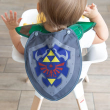 Load image into Gallery viewer, A toddler in a high chair faces away from the camera, showcasing the shield-shaped cape of Bumkins Caped SuperBib®: The Legend of Zelda™ Link.
