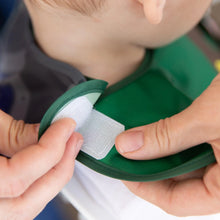 Load image into Gallery viewer, Close-up of hands adjusting the hook-and-loop closure of a Bumkins Caped SuperBib®: The Legend of Zelda™ Link around a child's neck.
