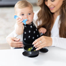 Load image into Gallery viewer, A baby with in a bib holds a Bumkins Silicone Dipping Spoons: Mickey Mouse (Black and Blue), while an adult feeds them from a bowl.
