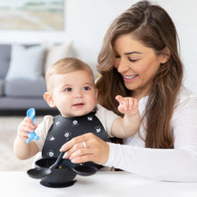 Load image into Gallery viewer, A baby in a bib sits on a woman's lap as she feeds them with a Bumkins Silicone Dipping Spoons: Mickey Mouse (Black and Blue) from a bowl.
