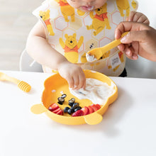 Load image into Gallery viewer, A baby in a bib reaches for fruit and yogurt on a yellow bear plate, aided by an adult with Bumkins Silicone Dipping Spoons: Winnie the Pooh.
