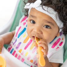 Load image into Gallery viewer, A baby with curls, wearing a white headband and colorful bib, chews a yellow Bumkins Silicone Dipping Spoons 3 Pack: Tutti-Frutti.
