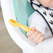 Load image into Gallery viewer, Close-up of a baby in a patterned bib in a high chair, holding a yellow Bumkins Silicone Dipping Spoons 3 Pack: Tutti-Frutti.
