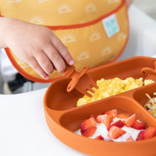 Load image into Gallery viewer, Close-up of a child using Bumkins Silicone Chewtensils®: Clay to pick up eggs from a divided plate, with strawberries and yogurt nearby.
