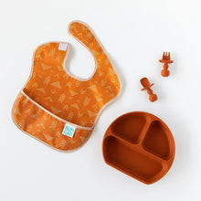 Load image into Gallery viewer, Bumkins Silicone Chewtensils®: Clay sits next to a matching plate and an orange bib with an abstract print on a white background.
