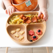 Load image into Gallery viewer, A baby uses Bumkins Silicone Chewtensils®: Clay to eat from a plate with pasta, fruit flowers, and animal crackers on a high chair tray.
