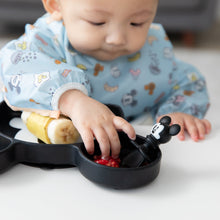 Load image into Gallery viewer, A boy in a blue bib reaches for a Bumkins Silicone Chewtensils®: Mickey Mouse sitting on a Mickey Mouse-shaped plate with fruit.
