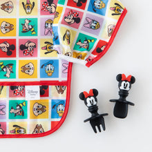 Load image into Gallery viewer, Close-up of Bumkins Silicone Chewtensils®: Minnie Mouse next to a colorful Disney character print bib on a white background.

