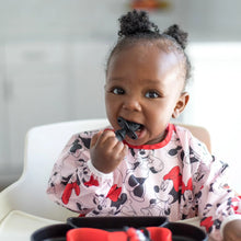 Load image into Gallery viewer, A toddler in a Minnie Mouse bib is happily chewing on a Bumkins Silicone Chewtensils®: Minnie Mouse in a high chair.
