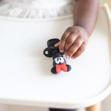 Load image into Gallery viewer, A young child in a white shirt holds a Bumkins Silicone Chewtensils®: Minnie Mouse.
