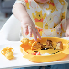 Load image into Gallery viewer, Close-up of a baby in a high chair reaching for food on a yellow bear plate with Bumkins Silicone Chewtensils®: Winnie The Pooh nearby.
