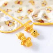 Load image into Gallery viewer, Close-up of Bumkins Silicone Chewtensils®: Winnie The Pooh on a white background with a yellow sleeved bib blurred behind.

