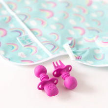 Load image into Gallery viewer, Bumkins Silicone Chewtensils®: Fuchsia  sits in front of a rainbow-print sleeved bib on a white background; the spoon sits face-down.
