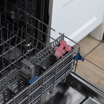 Bumkins Silicone Chewtensils®: Pink Jelly  sit in the utensil compartment of an open dishwasher.