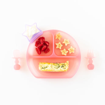 Bumkins Silicone Chewtensils®: Pink Jelly sit by a pink divided plate with quiche, fruit, and yogurt in a star cup on a white background.