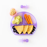 Bumkins Silicone Chewtensils®: Purple Jelly sit near a purple divided plate with tortillas, beans, veggies & hummus on a white background.