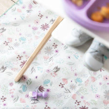 Load image into Gallery viewer, A floral mat with a Bumkins Silicone Chewtensils®: Lavender sits under a high chair; a child's shoes and a divided plate are blurred above.
