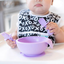 Load image into Gallery viewer, Close-up of a baby in a high chair, wearing a black &amp; white bib as they eat from a purple bowl with Bumkins Silicone Chewtensils®: Lavender.
