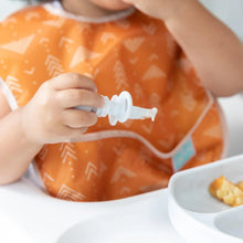 Load image into Gallery viewer, Close-up of a toddler in an orange bib gripping a Bumkins Silicone Chewtensils®: Marble with a matching plate of food nearby.
