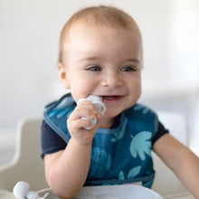 Load image into Gallery viewer, A smiling baby in a high chair wearing a blue bib chews a Bumkins Silicone Chewtensils®: Marble.
