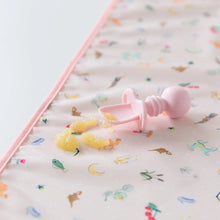 Load image into Gallery viewer, Close-up of a Bumkins Silicone Chewtensils®: Pink with applesauce splatter on a pink waterproof mat on a white background.
