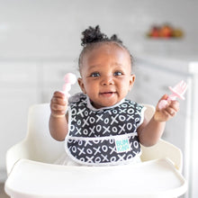 Load image into Gallery viewer, A smiling baby in a high chair wearing a black &amp; white bib holds Bumkins Silicone Chewtensils®: Pink.
