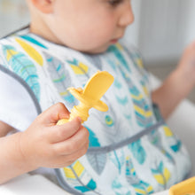Load image into Gallery viewer, A young child in a colorful bib holds a Bumkins Silicone Chewtensils®: Pineapple.
