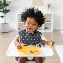 Load image into Gallery viewer, A toddler sits in a high chair, wearing a black patterned bib and eating from a yellow plate with Bumkins Silicone Chewtensils®: Pineapple.
