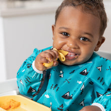 Load image into Gallery viewer, A baby in a high chair smiles with a Bumkins Silicone Chewtensils®: Pineapple near their mouth, wearing a blue patterned bib.
