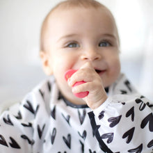 Load image into Gallery viewer, A smiling baby wears a heart-patterned bib, chewing a Bumkins Silicone Chewtensils®: Red.
