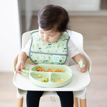 Load image into Gallery viewer, A toddler in a high chair wearing a green bib holds Bumkins Silicone Chewtensils®: Sage near a matching plate with food.
