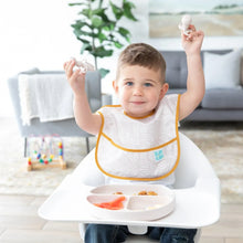 Load image into Gallery viewer, A toddler in a high chair holds Bumkins Silicone Chewtensils®: Sand, enjoying baby-led weaning, with toys scattered on the floor.
