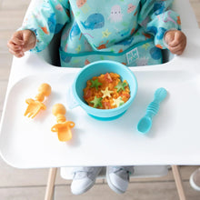 Load image into Gallery viewer, A child sits in a high chair wearing a blue bib, with a blue bowl of food, spoon, and Bumkins Silicone Chewtensils®: Tangerine on the tray.
