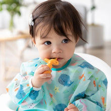 Load image into Gallery viewer, A toddler in a blue sea animal-themed bib chews a Bumkins Silicone Chewtensils®: Tangerine.
