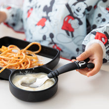Load image into Gallery viewer, A boy in a Mickey Mouse sleeved bib uses Bumkins Spoon + Fork: Mickey Mouse to eat a meal with a Mickey Mouse Grip Dish at a white table. 

