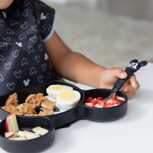 Load image into Gallery viewer, Close-up of a child holding a Bumkins Spoon + Fork: Mickey Mouse, eating from a Mickey-shaped plate with waffles, eggs, and fruit.
