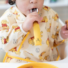 Load image into Gallery viewer, Close-up of a child in a yellow bear-patterned bib holding a Bumkins Spoon + Fork: Winnie the Pooh in their mouth.

