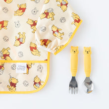 Load image into Gallery viewer, Bumkins Spoon + Fork: Winnie the Pooh sits next to a yellow Winnie the Pooh patterned bib on a white background.
