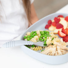 Load image into Gallery viewer, Close-up of a child with a gray plate of pasta, peas, chicken and berries with a Bumkins Spoon + Fork: Gray on a white table.
