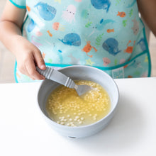 Load image into Gallery viewer, Close-up of a child in a blue whale-print bib eating soup from a bowl with Bumkins Spoon + Fork: Gray at a white table.
