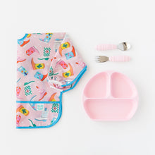 Load image into Gallery viewer, Bumkins Spoon + Fork: pink rests near a pink Grip Dish and a colorful sleeved bib with a boot print, on a white background.
