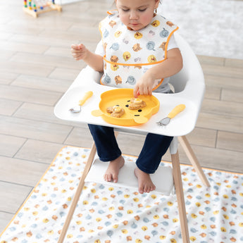A toddler in a high chair eats from a bear-shaped plate, with Bumkins Spoon + Fork: Pineapple on the tray nearby.